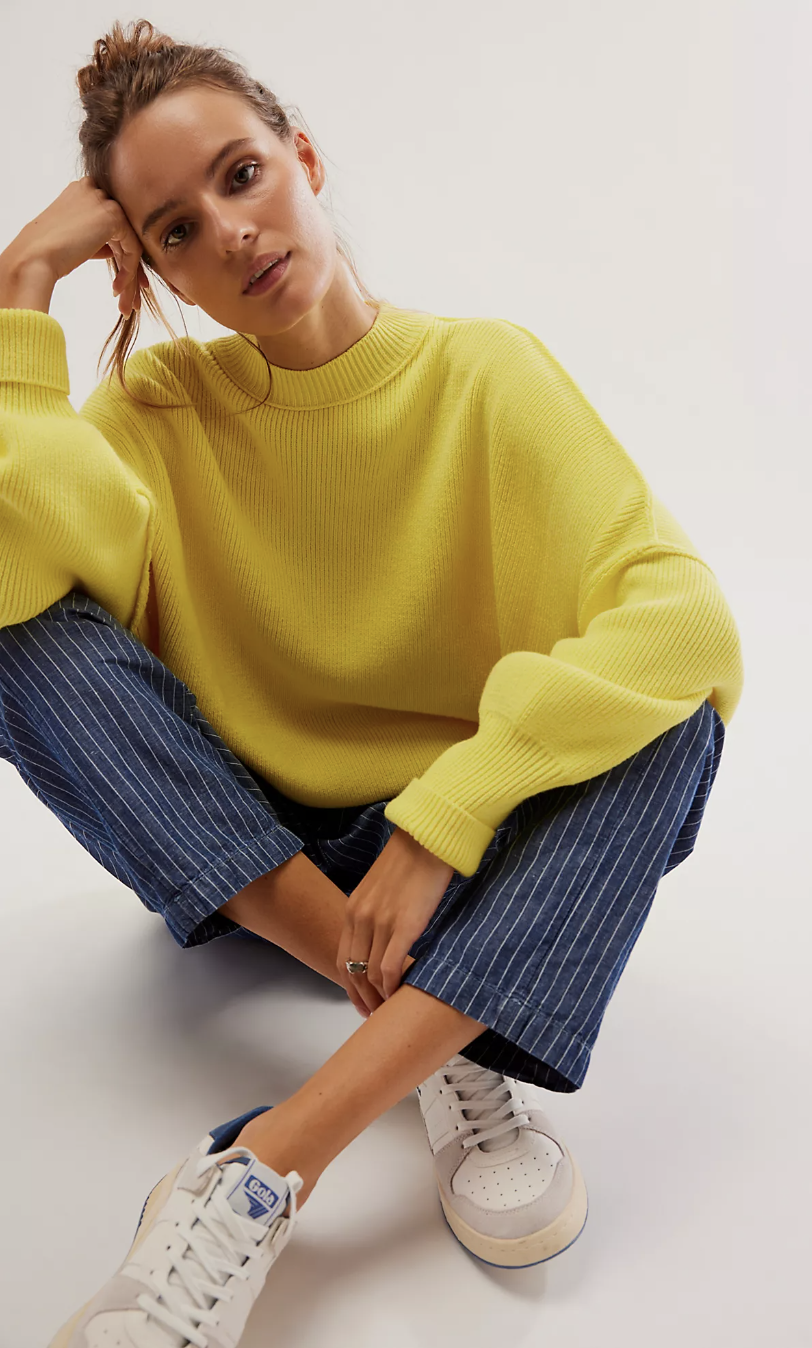a white woman sits on the ground wearing a light yellow sweater