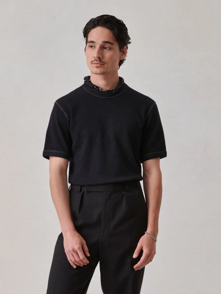 A dark-haired man modeling a dark tee shirt with dark pants.