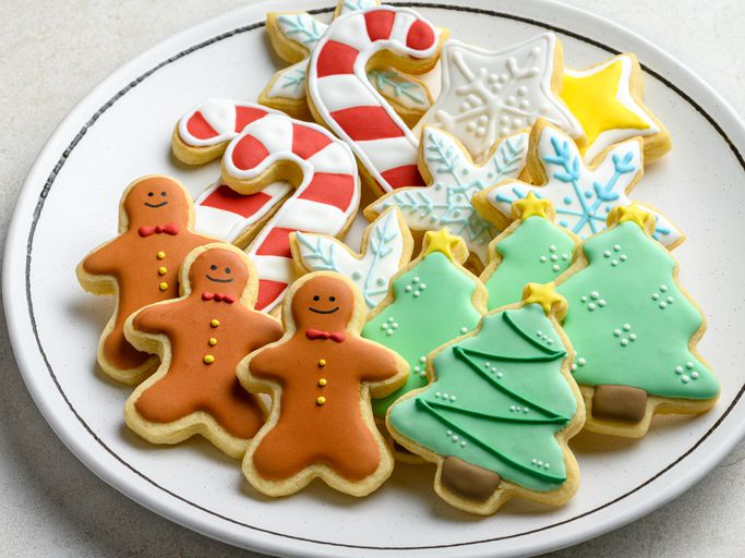 A plate full of decorated soft cookies like candy canes, Christmas trees, and gingerbread men.