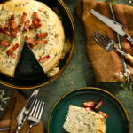 An aerial view of a Savory Zucchini Crepe Cake on a black plate with a slice cut out of it. The slice sits on a smaller green plate to the right.
