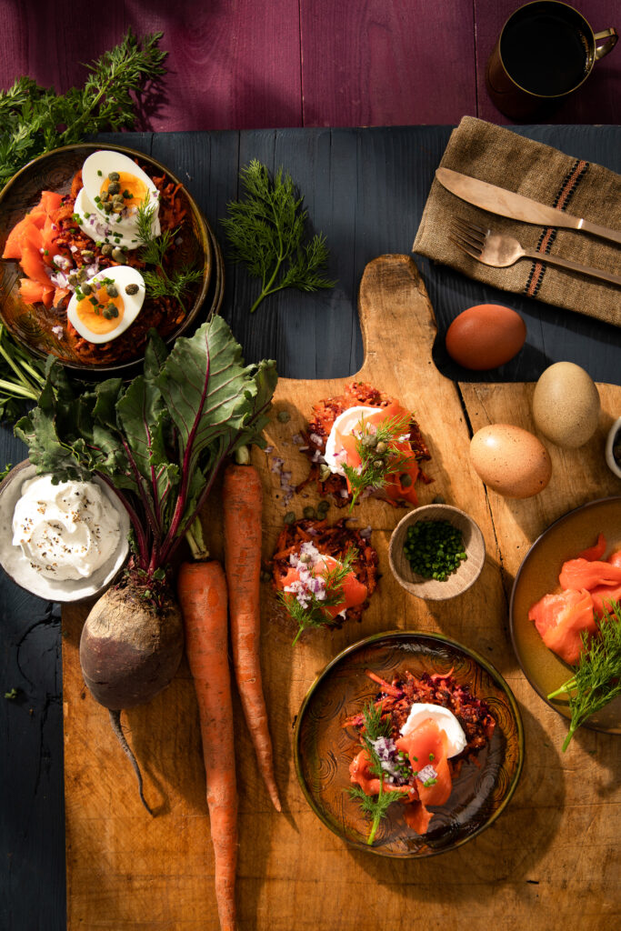 An aerial view of a wooden cutting board filled with various veggies like carrots and beets. Carrot and Beet Latkes recipe