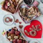 An aerial shot of a valentines day dessert spread with reds, pinks, and Whole Grain Sour Cherry Jam Shortbread Bars in the shapes of hearts and L O V E.