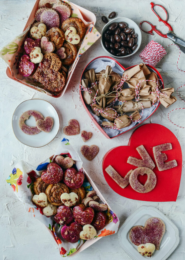 An aerial shot of a valentines day dessert spread with reds, pinks, and Whole Grain Sour Cherry Jam Shortbread Bars in the shapes of hearts and L O V E.