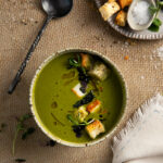 An aerial shot of a green soup in a small ceramic bowl. A black spoon sits to the left side. Kale Soup Recipe