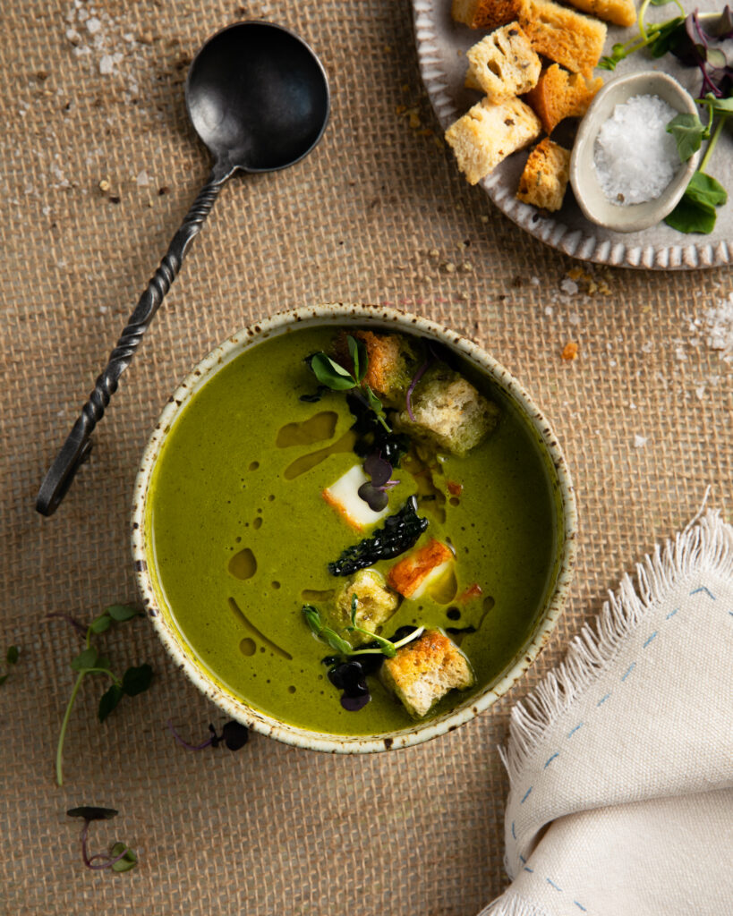 An aerial shot of a green soup in a small ceramic bowl. A black spoon sits to the left side. Kale Soup Recipe