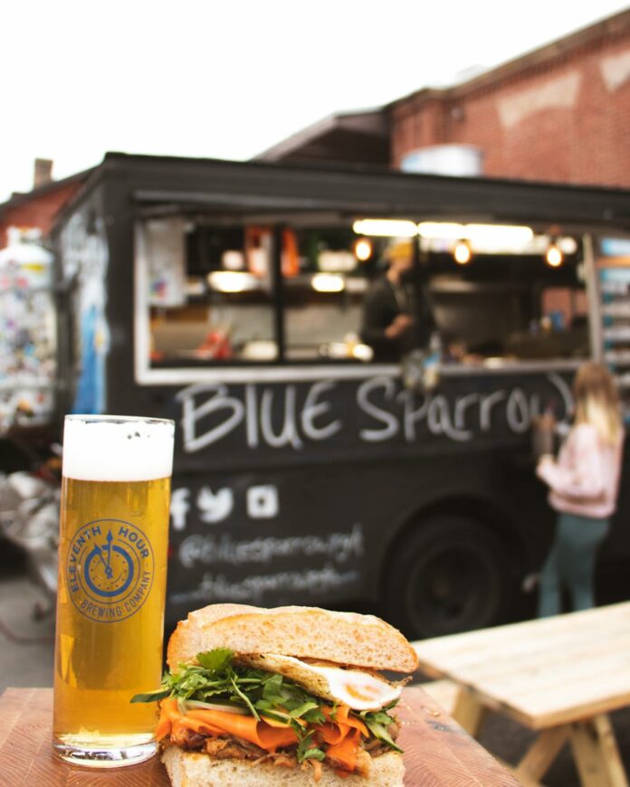 A beer and a sandwich sit in front of the Blue Sparrow food truck