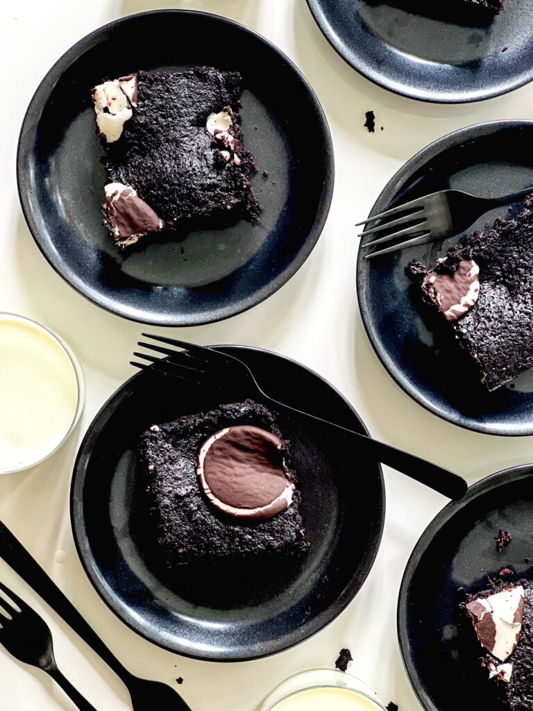 An aerial shot of four black plates, each with a piece of Fudgy Peppermint Patty Brownies sitting on them. Fudgy Peppermint Patty Brownies recipe