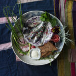 Pickled herring plated on a blue backdrop with spiced garnishes.