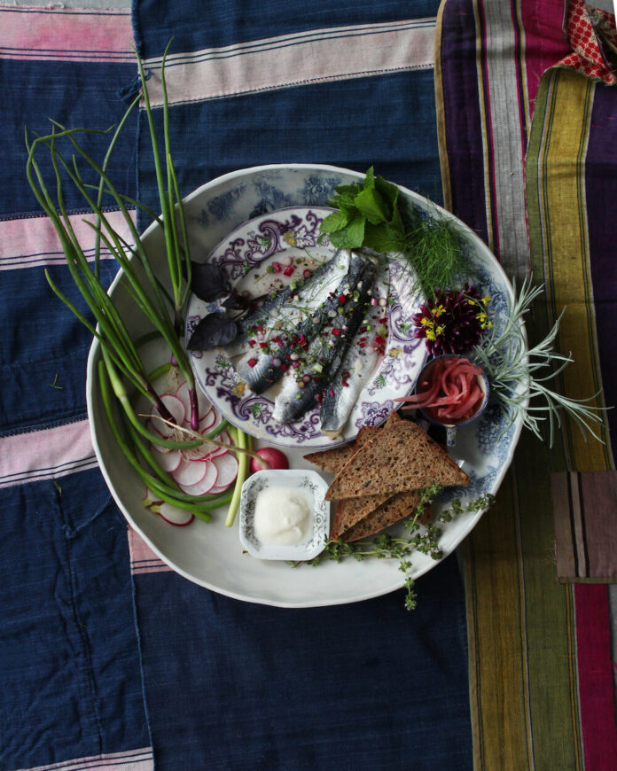 Pickled herring plated on a blue backdrop with spiced garnishes.