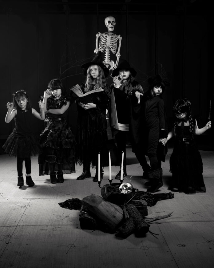 Six little girls dressed in black costumes with a skeleton behind them.