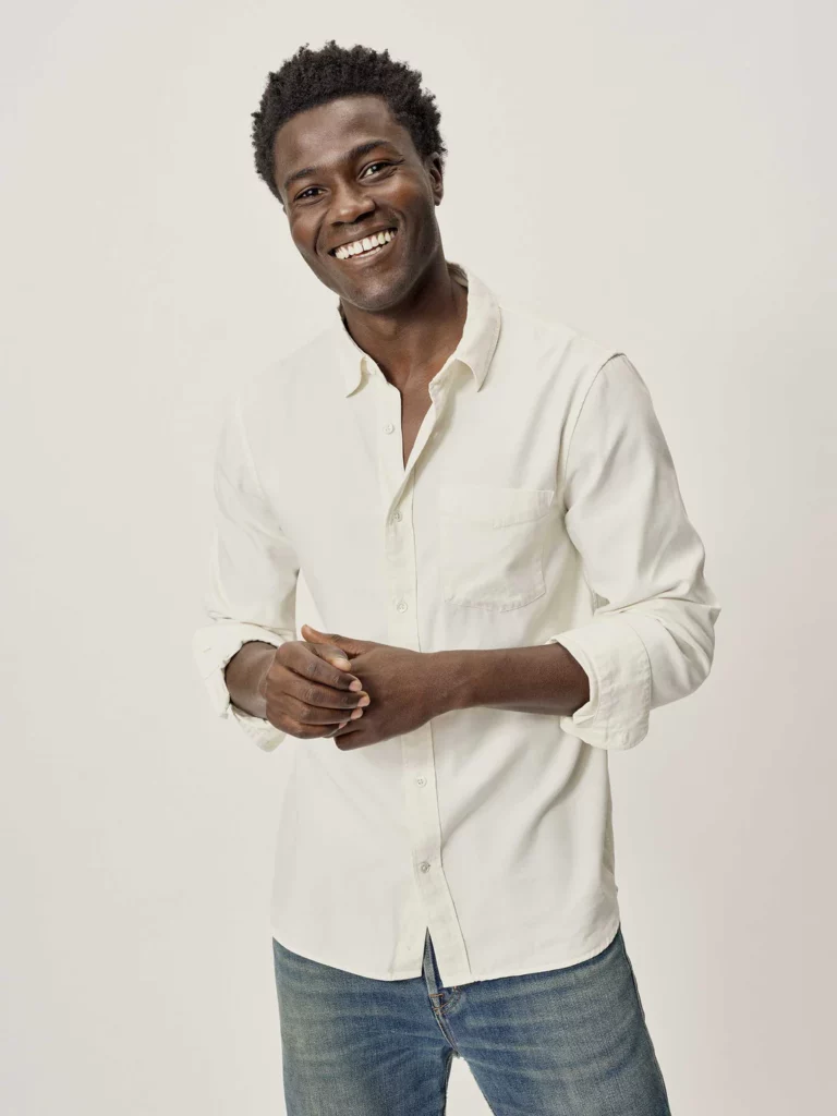 A black-haired man models a white twill shirt with one pocket and blue jeans.