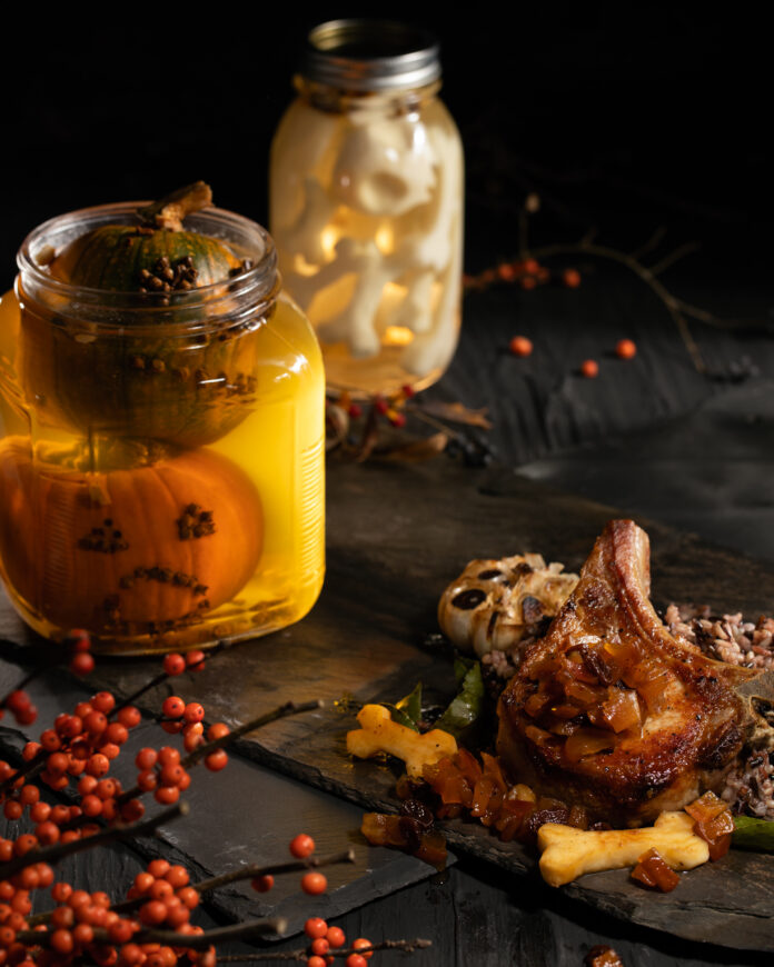 A glass jar with Pickled Pumpkin Heads in a dark setting, meat and bones sit off to the left. pickled pumpkin recipe