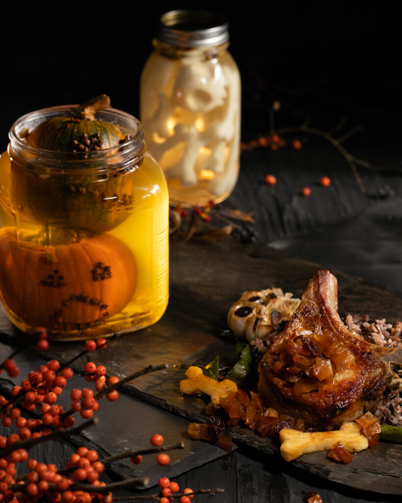 A glass jar with Pickled Pumpkin Heads in a dark setting, meat and bones sit off to the left. pickled pumpkin recipe