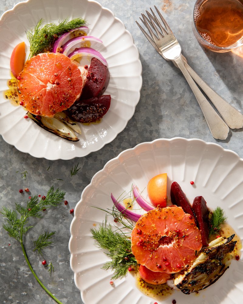 A pickled vegetable salad plated on white plates with silverwear.