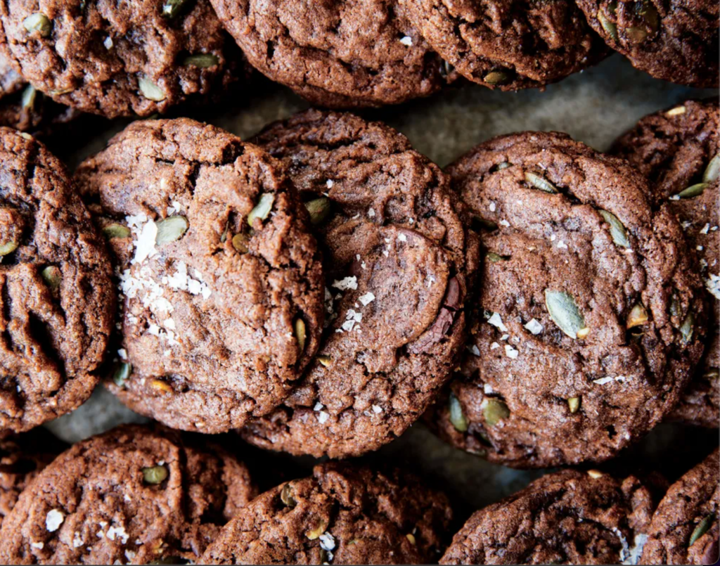 Chocolate pumpkin seed cookies are laid out on a table.