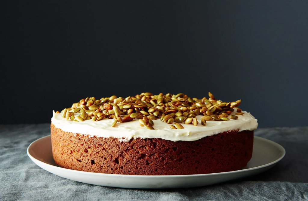 A cake topped with cream cheese frosting and pumpkin seeds on a plate.