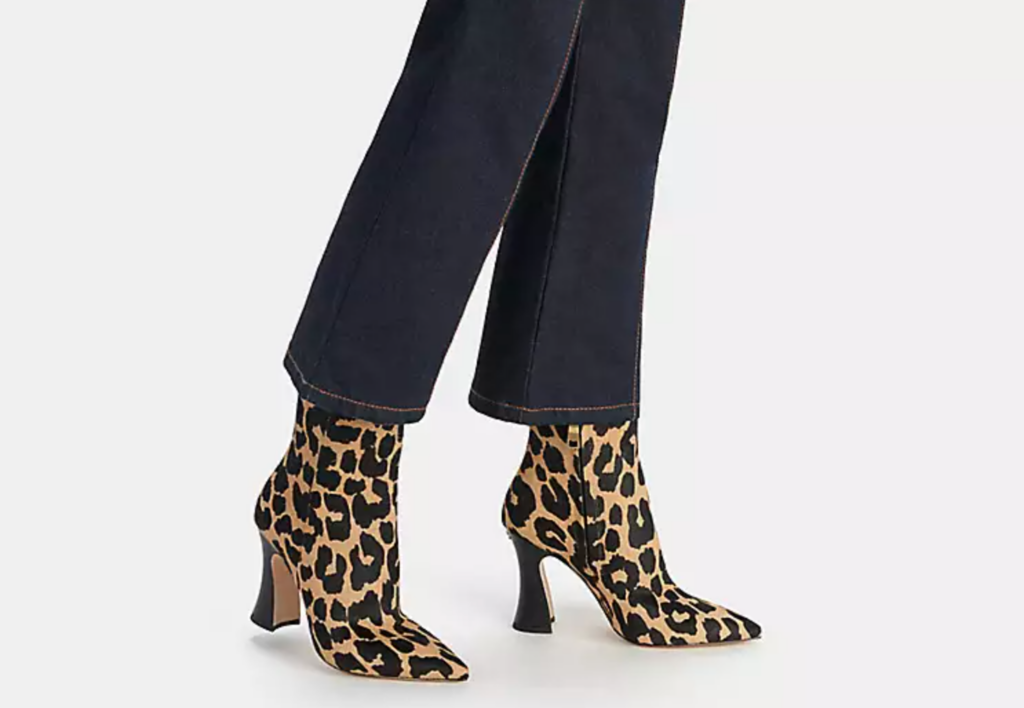 A women models a set of leopard print heeled boots on a white background.