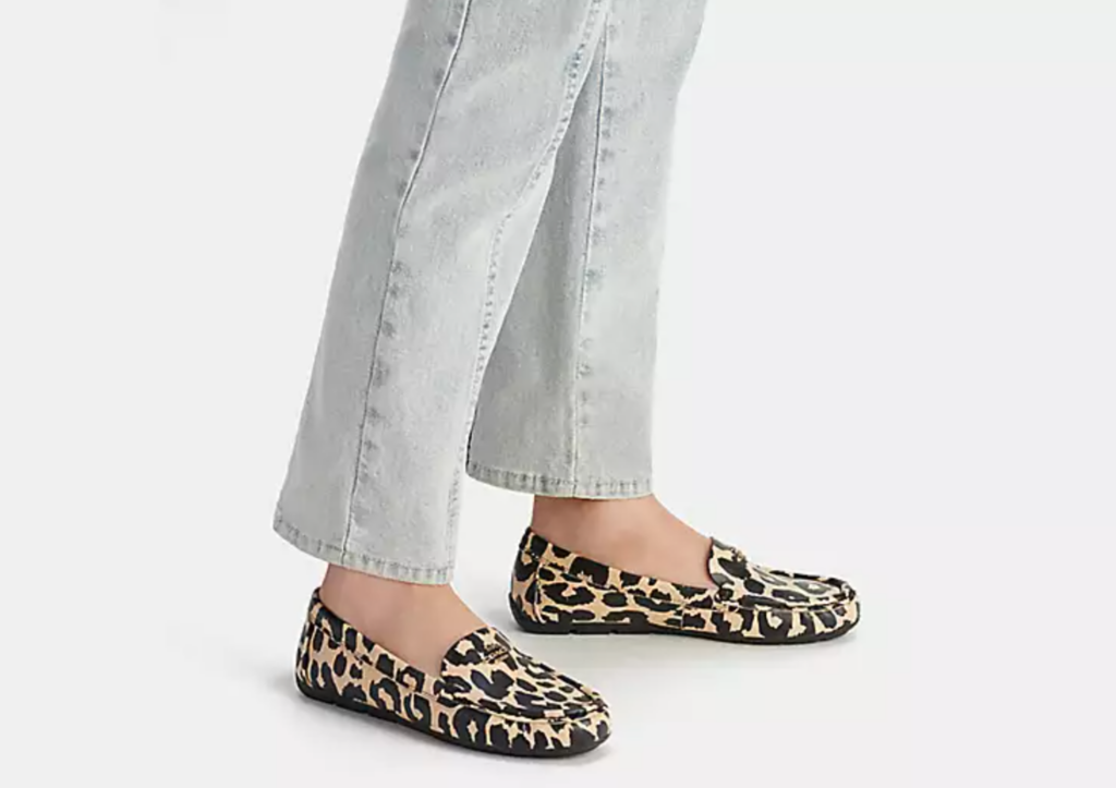 A woman models a pair of leopard print flats with grey pants.