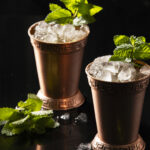 two cocktails in metal rocks cups, garnished with mint. mint julep recipe