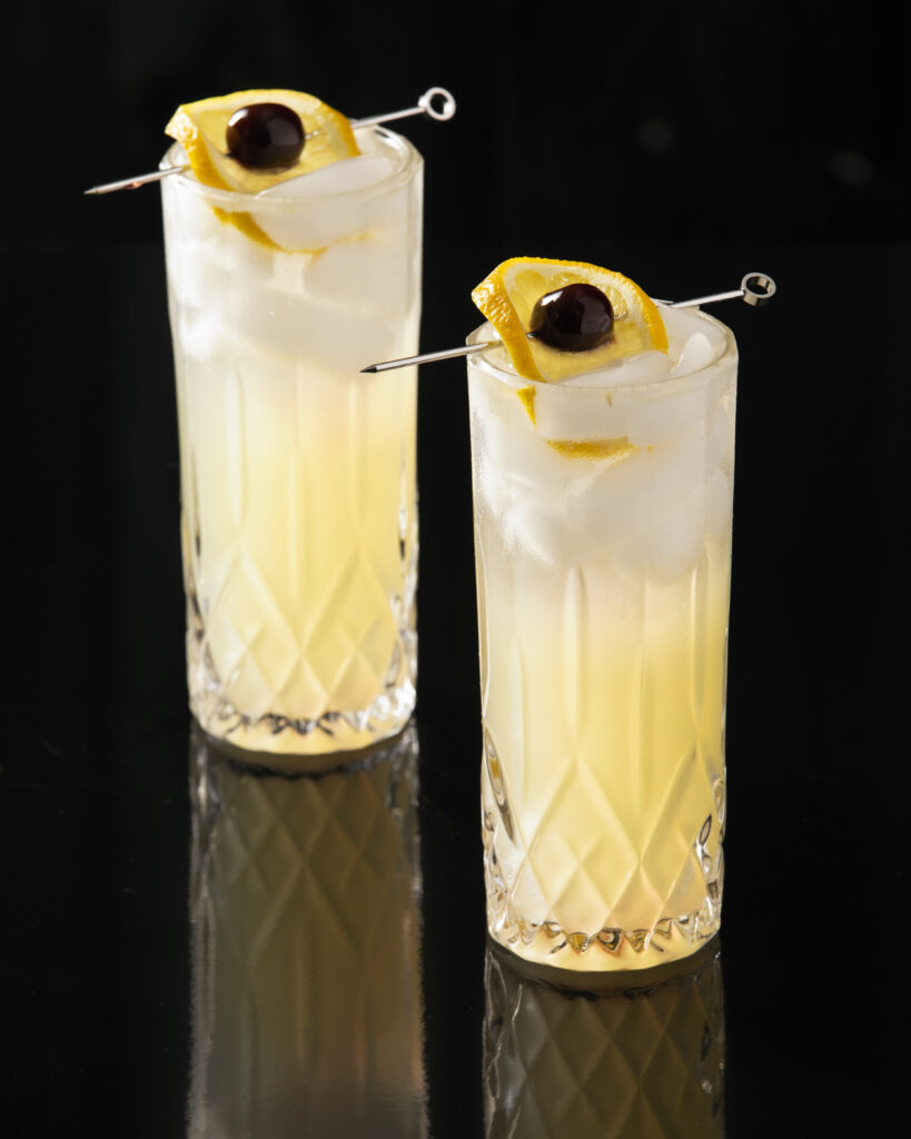Two beverages in tall glasses, light yellow in color. Tom Collins cocktail