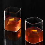 Two cocktails brown in color in square rocks glasses