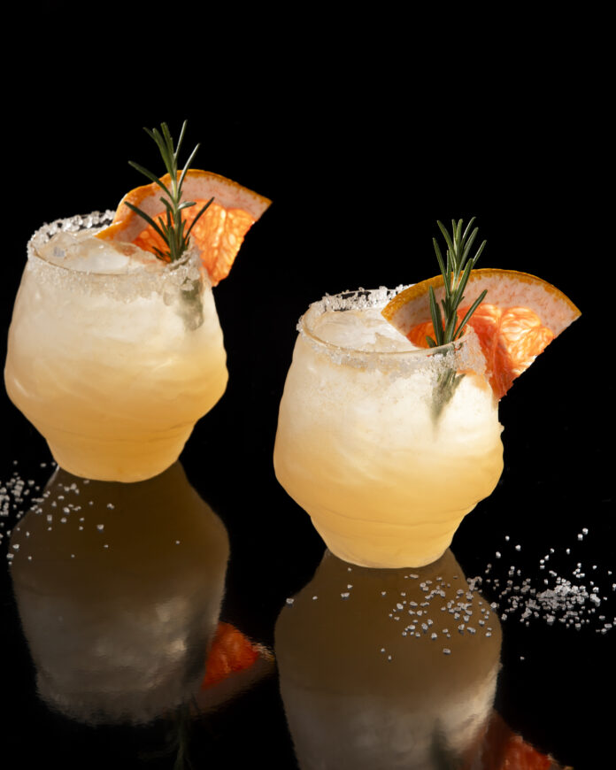 Two light orange drinks garnished with Grapefruit Wedges. Paloma Cocktail