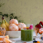 A green liquid sits in a small clear glass surrounded by various fruits and nuts. green smoothie recipe