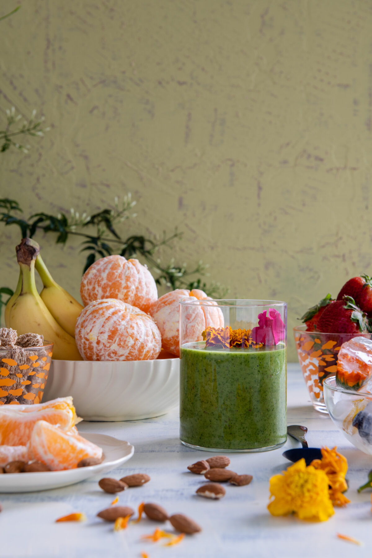 A green liquid sits in a small clear glass surrounded by various fruits and nuts. green smoothie recipe