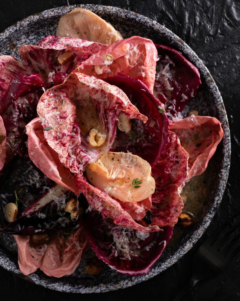 Varigated purple lettuces on a dark speckled plate with a creamy dressing and chopped nuts.