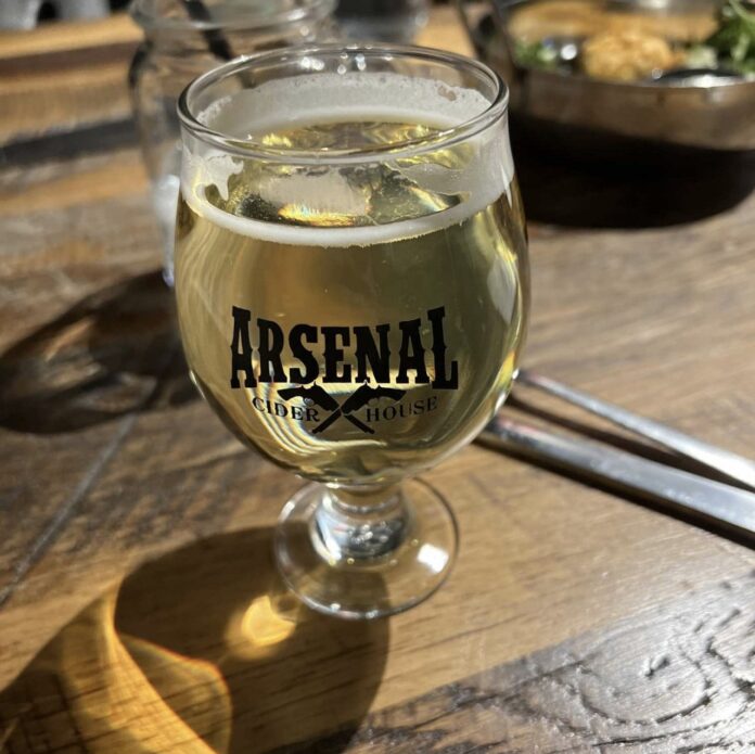 A glass of cider in an Arsenal Cider House cup on a wooden table.