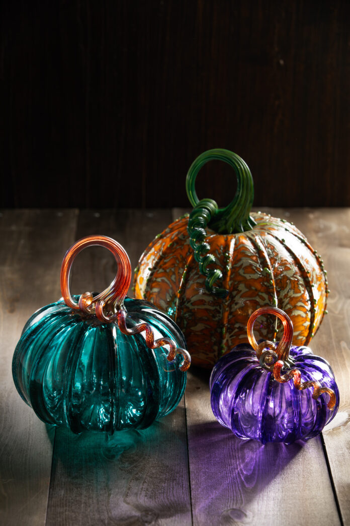 Colorful, glass-blown pumpkins with twisty stems on a wood backdrop.