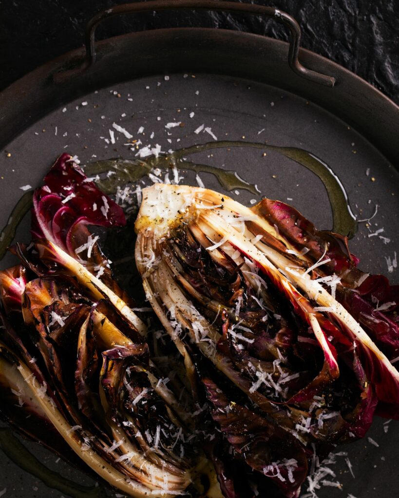 A head of radicchio cut in half and charred on a dark plate with shaved parmesan.