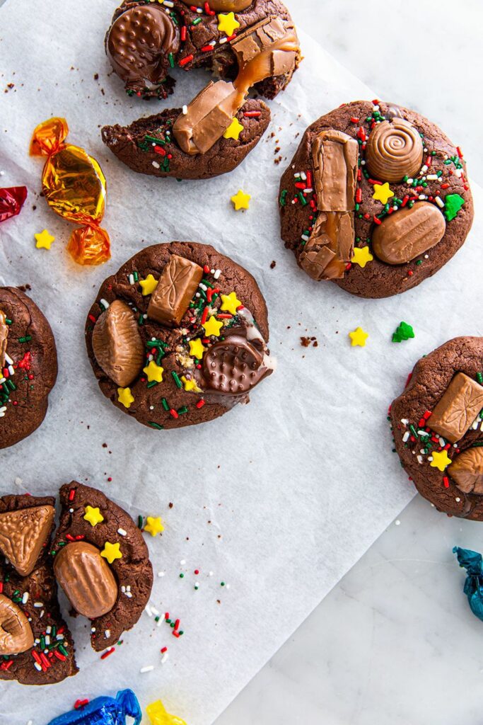 An array of chocolate cookies coated in tiny chocolates laid out on a street of parchment paper and topped with star sprinkles.