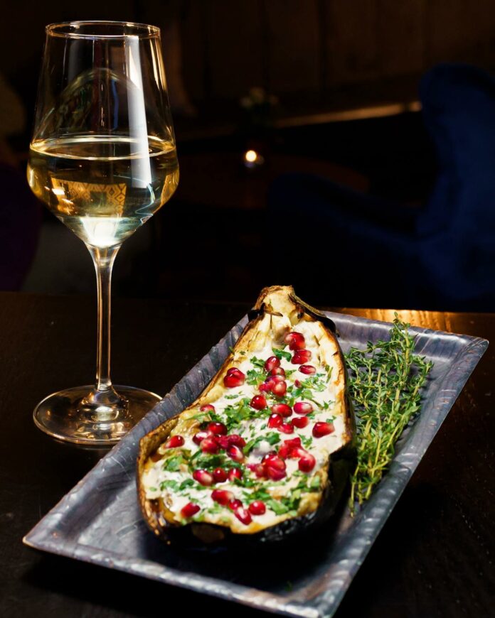 A glass of white wine sits next to a flatbread on a silver rectangle plate. Lawrenceville restaurant