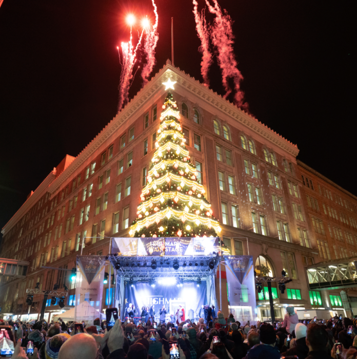 The Pittsburgh Highmark building lit up with a Christmas Tree on the corner, fireworks in the sky, and a stage on the ground.