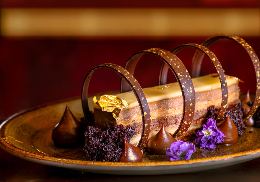 A chocolate coffee crunch log surrounded by edible flowers, chocolate kisses, and four chocolate rings on a plate.