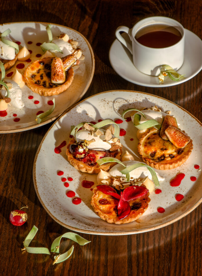 Two plates each with a trio of clafouti decorated with red and green garnish, and sitting near a cup of tea