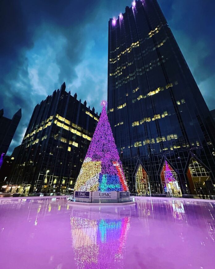 A lit up Christmas tree stadfs in the center of the PPG ice rink surrounded by Downtown Pittsburgh Restaurants.
