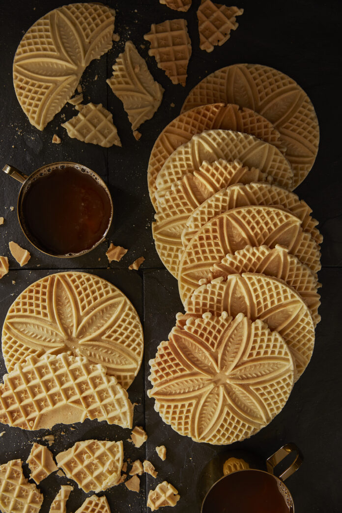 Various Pizzelles laid out on a table with flower shapes in each.