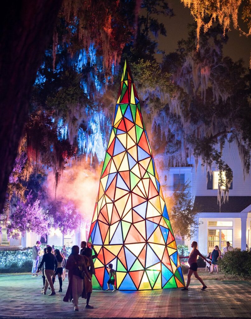 A colorful stained glass Christmas tree stands in the center of holiday lights.