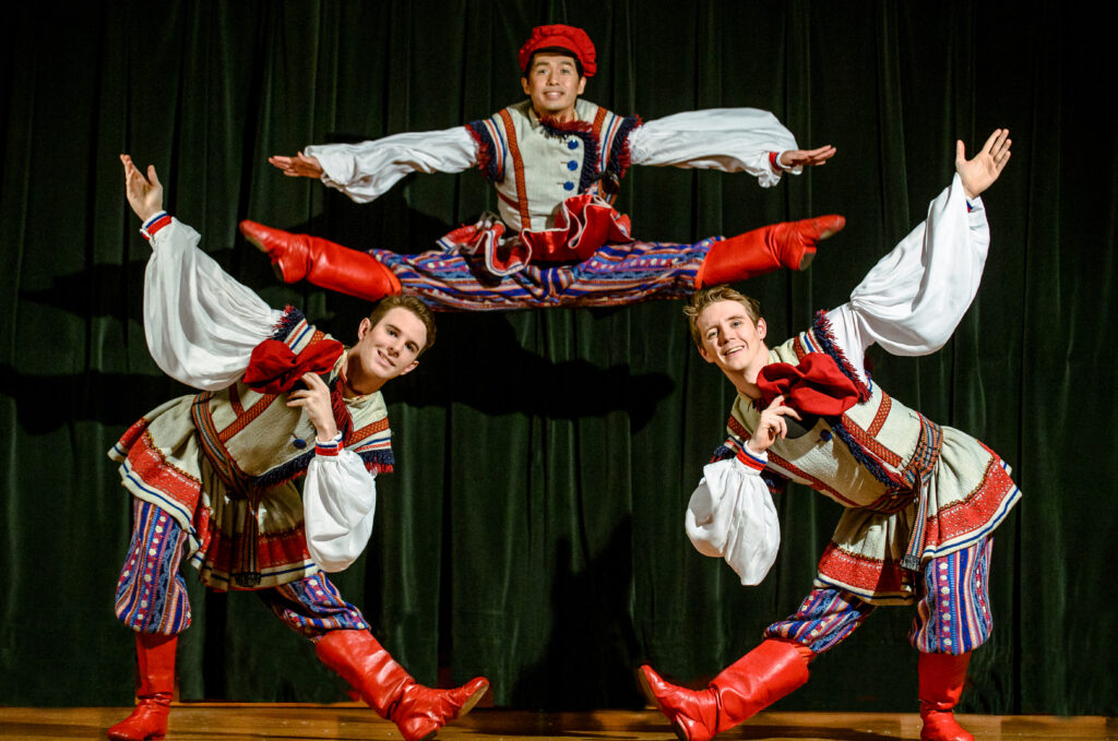 Three dancers in red, blue, and white outfits