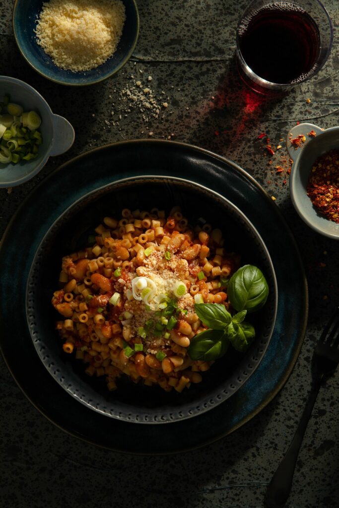 A black bowl filled with fresh Pasta Fagioli noodles and vegetables by Victoria Sande.