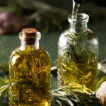 Two textured clear glass bottles with cork closure, filled with homemade herb-infused olive oil made with dried rosemary, thyme, and oregano.