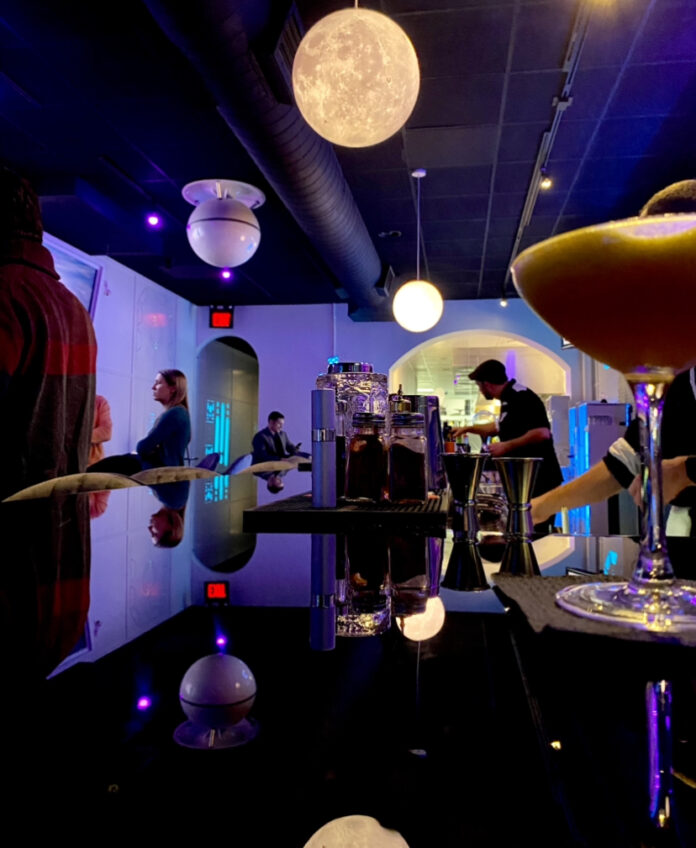 A reflective black bar at Space Bar in Market Square sits beneath a moon light with a cocktail on the right side.
