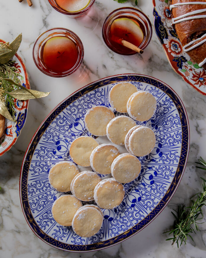 A blue patterned plate filled with little sweets with three orangish glasses above the plate.