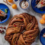 A braided bread with berries and other seasonings inside it, surrounded by small blue plates and various ingredients.