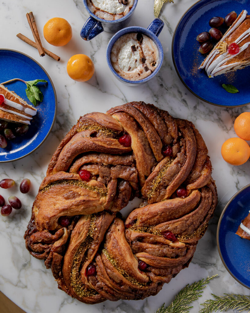 A braided bread with berries and other seasonings inside it, surrounded by small blue plates and various ingredients.