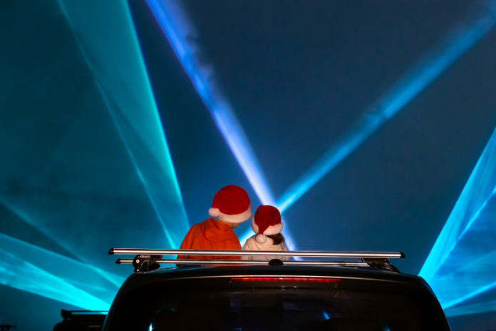 A rear view of two people with Santa hats sitting in a convertible car watching a laser light show.