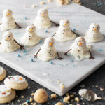 Melted Snowmen Cake Pops served on a white ceramic plate with cookies and crumbs in the surroundings