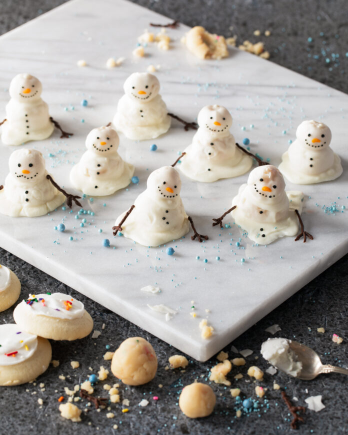 Melted Snowmen Cake Pops served on a white ceramic plate with cookies and crumbs in the surroundings